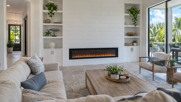 A long recessed electric fireplace with a glowing flame effect in a white shiplap wall between built-in shelves.